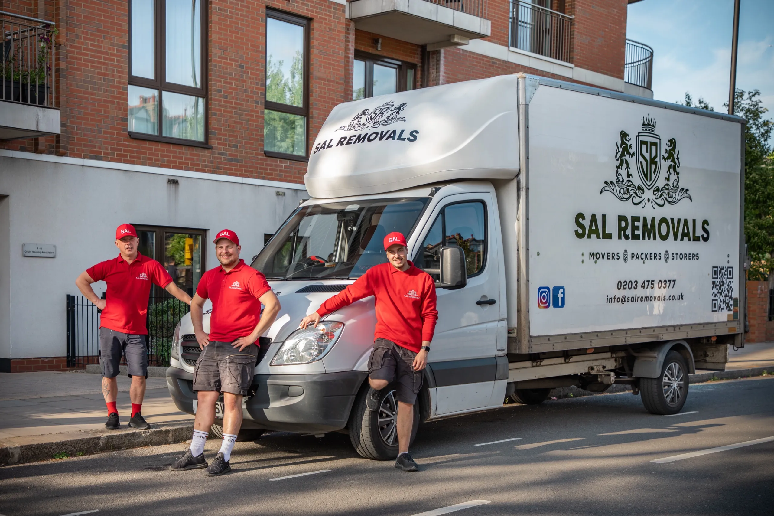 Three Sal Removals crew in red polo shirts beside a branded van