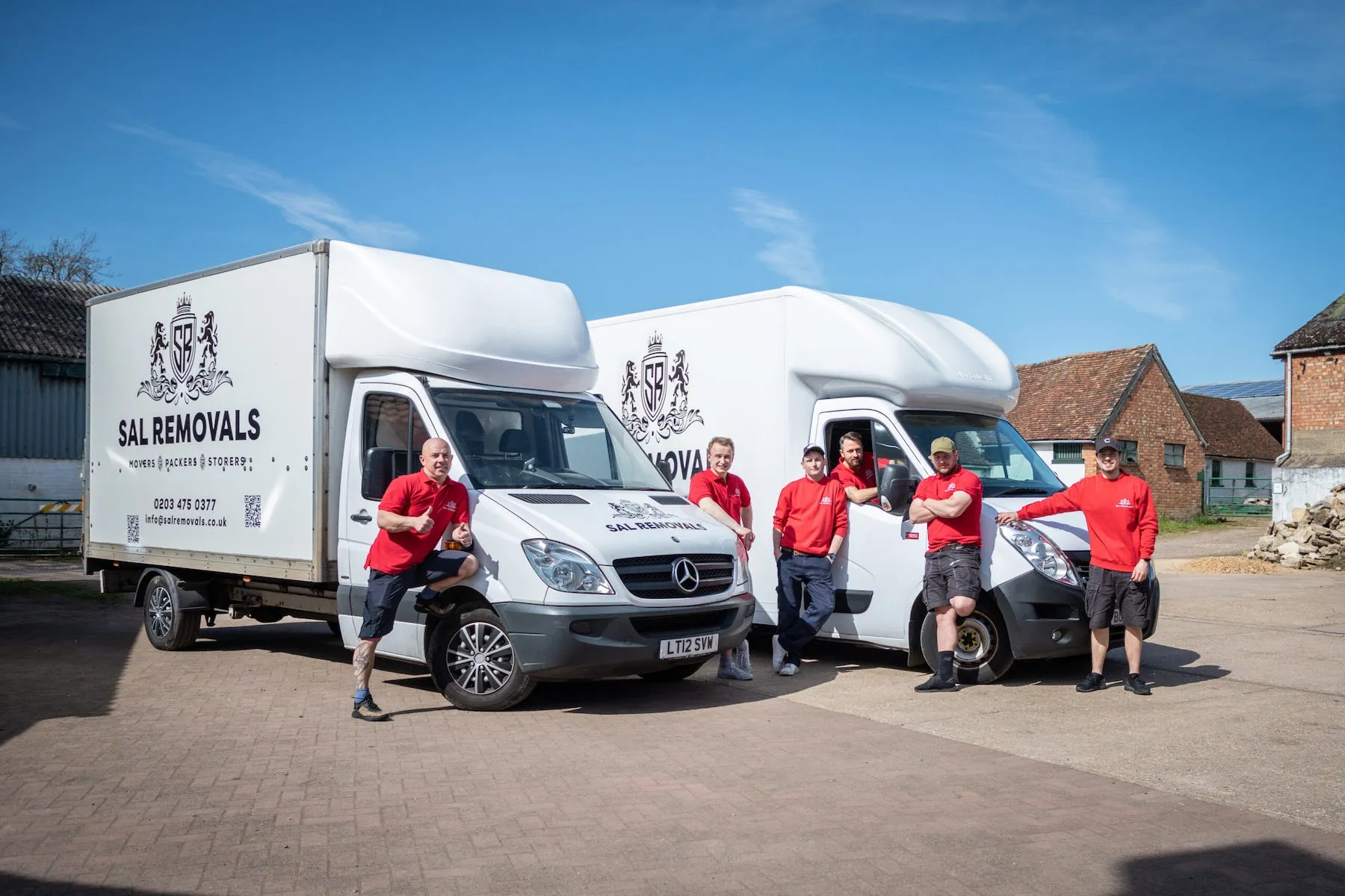Six Sal Removals crew with two branded Luton vans in the yard on a sunny day