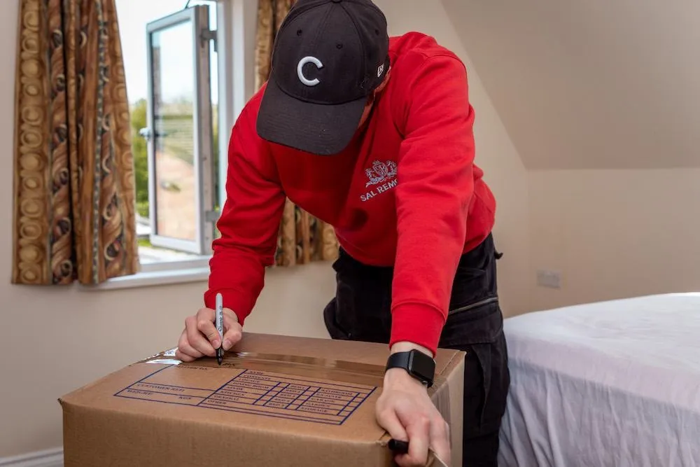 A Sal Removals team member in a red hoodie labelling a packed box in a bedroom