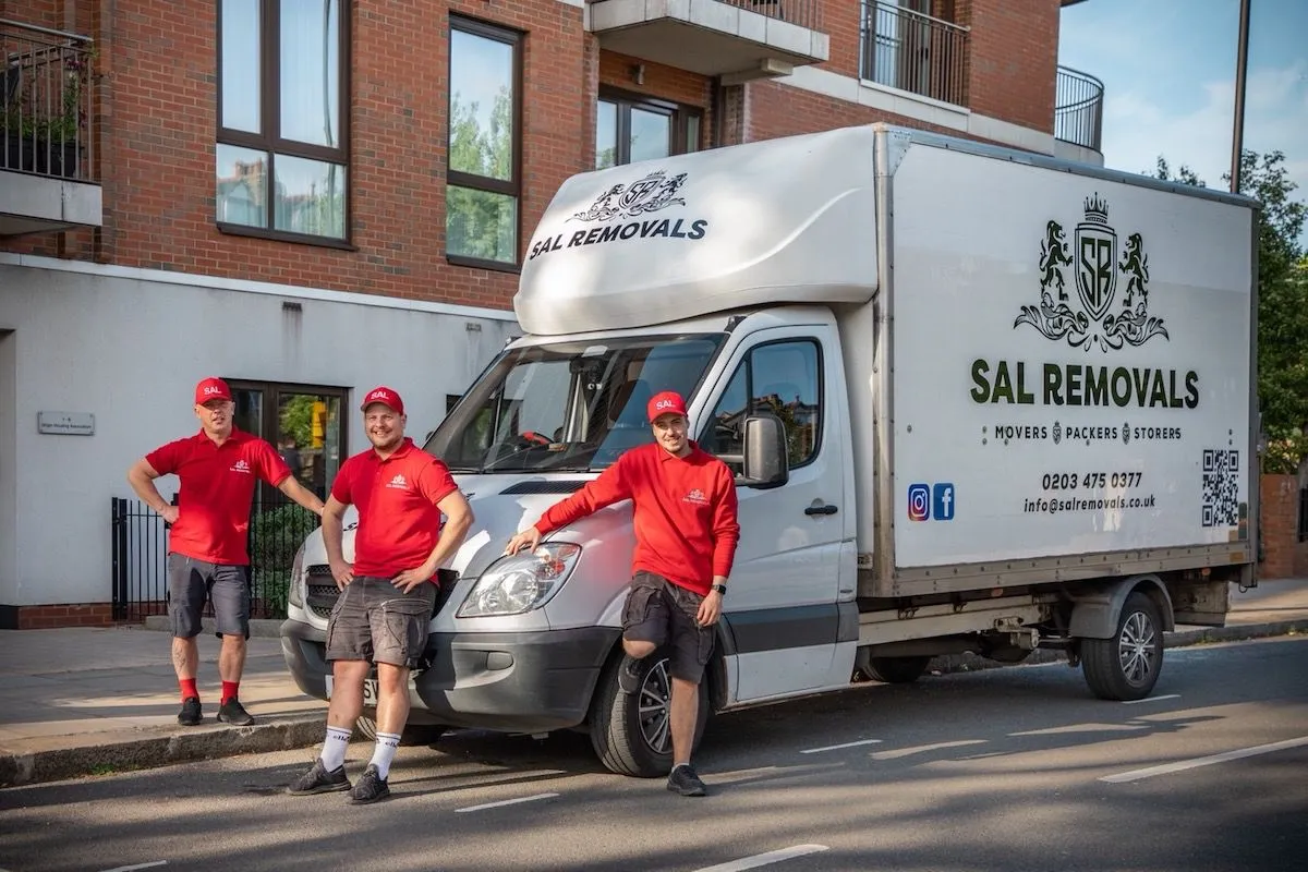 Three Sal Removals movers leaning on the front of a branded Luton van outside a block of flats